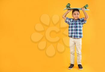 Portrait of cute little boy with skateboard on color background�