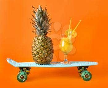 Ripe pineapple, skateboard and cocktail on color background�
