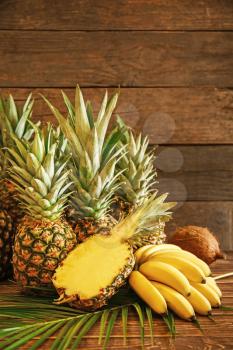 Ripe pineapples, bananas and coconut on wooden background�