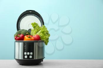 Modern multi cooker with vegetables on table against color background�