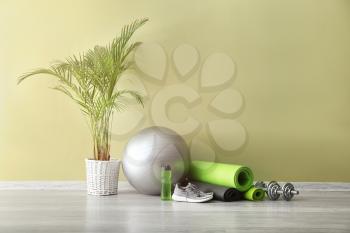 Set of sports equipment with fitness ball, bottle of water and shoes near color wall�
