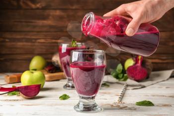 Woman pouring fresh beet smoothie into glass on table�