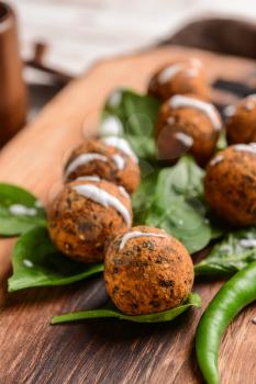Tasty falafel balls with chili and spinach on wooden board, closeup�