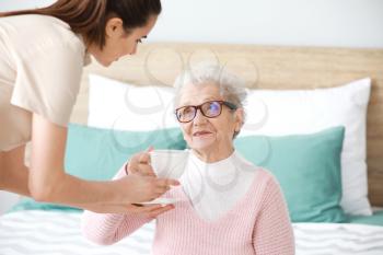 Caregiver serving tea for senior woman in nursing home�