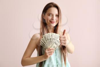 Young woman with money showing thumb-up on color background�