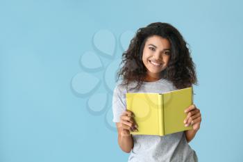 Portrait of happy African-American woman with book on color background�