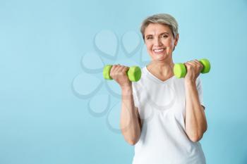 Sporty mature woman with dumbbells on color background�