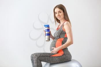 Beautiful sporty pregnant woman drinking water during training against grey background�