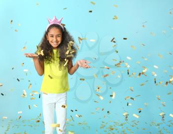 Cute African-American girl with crown and falling confetti on color background�