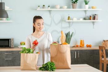 Beautiful woman with shopping bags full of fresh products in kitchen at home�