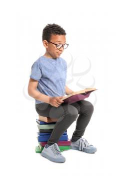 Cute African-American boy reading books on white background�