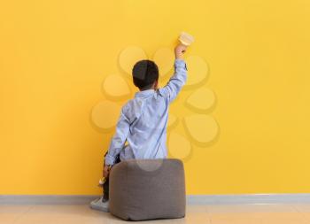 Cute African-American boy painting wall in room�