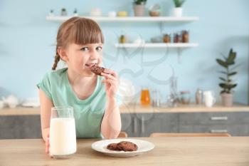 Cute little girl with glass of milk and cookies at table�