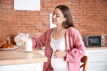 Beautiful pregnant woman drinking tasty milk in kitchen at home�