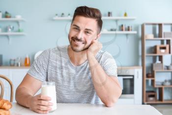 Handsome man drinking tasty milk in kitchen at home�