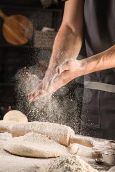 Man clapping hands and sprinkling flour over dough on table�