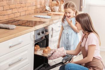 Little girl and her mother baking muffins in kitchen�
