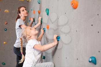 Young woman with her little daughter climbing wall in gym�