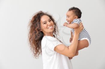 Happy African-American mother with cute little baby on light background�