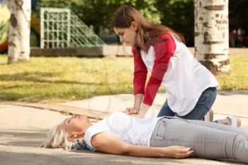 Female passer-by doing CPR on unconscious mature woman outdoors�