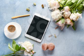 Beautiful peonies with tablet computer and cup of coffee on color background�