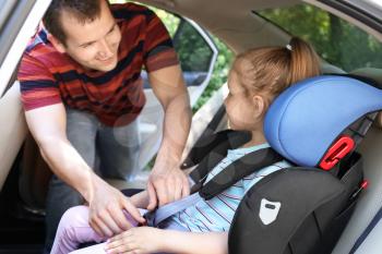 Father buckling his little daughter in car safety seat�