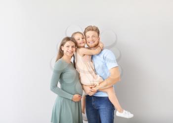 Beautiful pregnant woman with her family on light background�