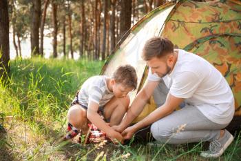 Father and his little son putting up camping tent in forest�