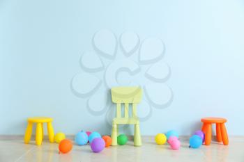 Chair, stools and balloons near color wall in children's room�