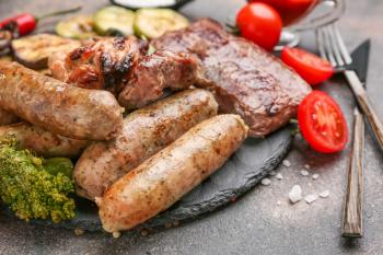 Slate plate with tasty grilled meat with sausages and vegetables on grey background�
