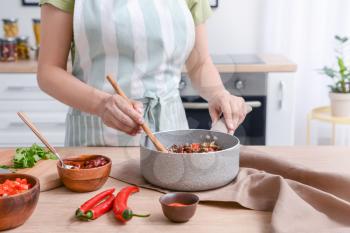 Woman cooking traditional chili con carne in kitchen�