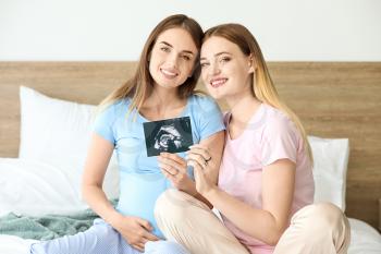 Pregnant lesbian couple with sonogram image in bedroom�