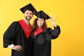 Young students in bachelor robes on color background�