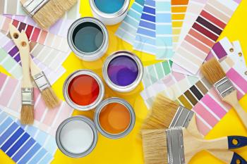 Cans of paints with brushes and palette samples on color background�