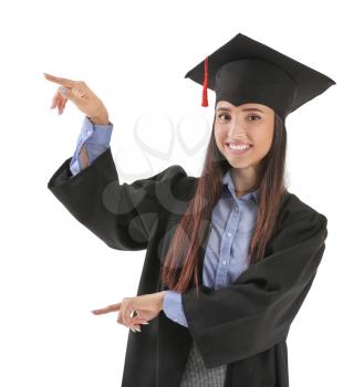 Female student in graduation cap and gown pointing at something on white background�
