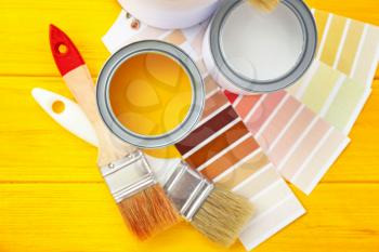 Cans of paint with brushes and palette samples on wooden background�
