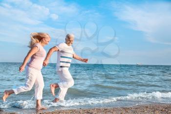 Happy mature couple running on sea beach�