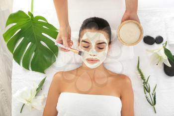 Cosmetologist applying mask on woman's face in spa salon�