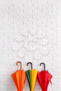 Stylish umbrellas near white brick wall�