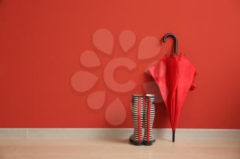 Stylish umbrella with gumboots near color wall�