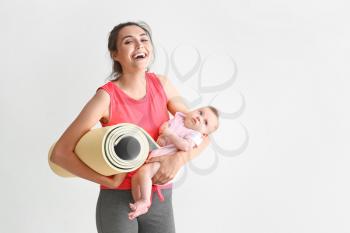 Mother with yoga mat and cute little baby on white background�