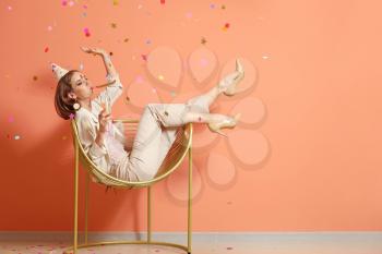 Happy woman with party whistle and glass of champagne near color wall�