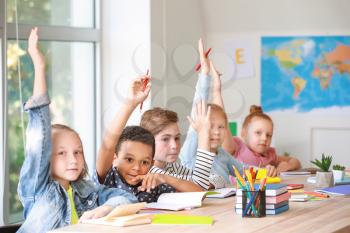Cute little pupils raising hands during lesson in classroom�
