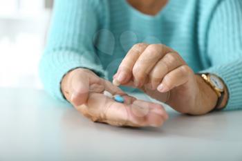 Elderly woman with pills at white table, closeup�