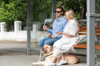 Blind young man with guide dog and mother waiting for bus outdoors�