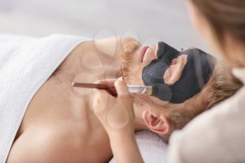 Cosmetologist applying mask on man's face in spa salon�