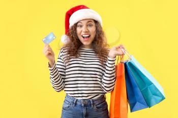Happy African-American woman in Santa hat, with credit card and shopping bags on color background�