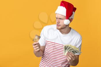 Stressed young man in Santa hat, with credit card and dollars on color background�