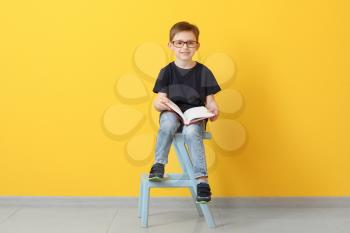 Little boy reading book near color wall�