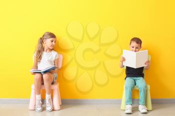 Little children with books sitting on chairs near color wall�